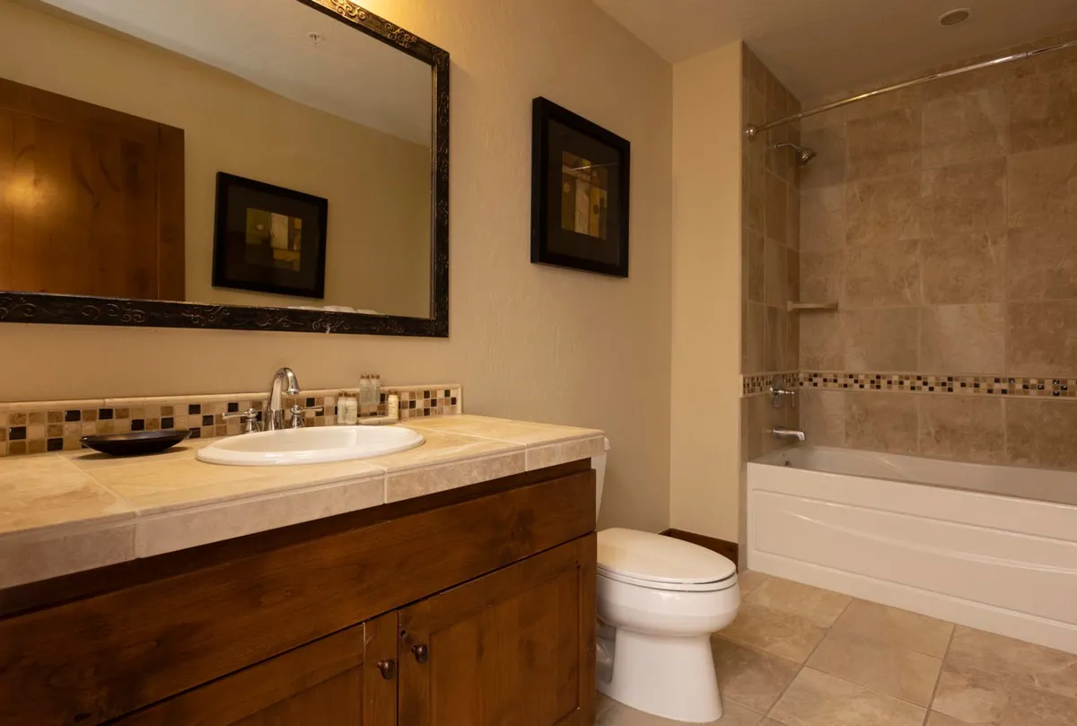A tranquil bathroom space featuring a deep bathtub, elegant sink, decorative tiles, and a large framed mirror. The soft lighting and serene design invite indulgent relaxation and self-care routines.