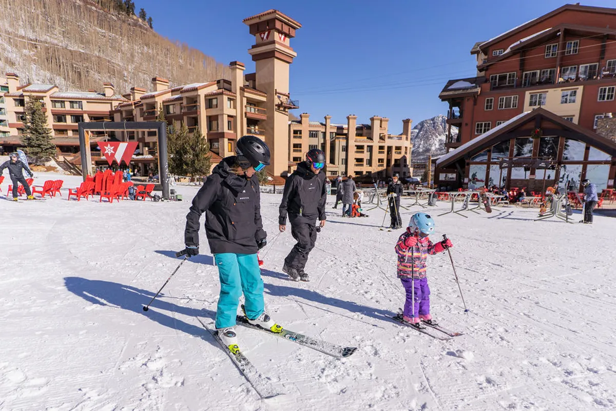 A lively scene featuring families and children gearing up for or enjoying skiing at the mountain resort base. The presence of ski equipment and young skiers highlights beginner-friendly opportunities and the joy of family outings in the snow.