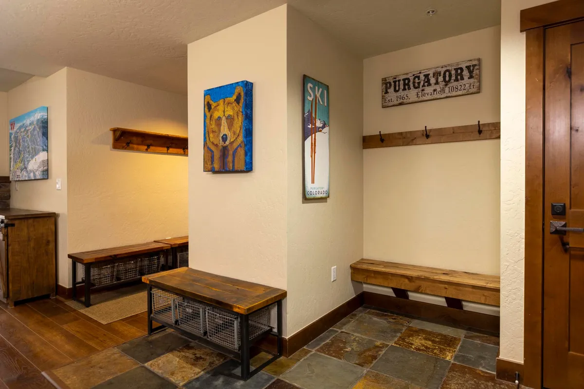 A cozy interior with wooden benches, a welcoming bear painting, ski-themed signage, and the Purgatory sign creates a sense of arrival and exclusivity for guests storing their ski gear or relaxing after a day outdoors.