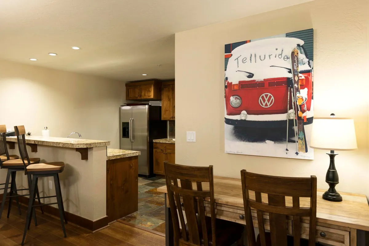 A stylish, open-plan dining and kitchen area with bar seating and a dining table set against playful VW van artwork. The scene feels social and functional, highlighting opportunities for both casual and celebratory meals in a cozy, inviting environment.